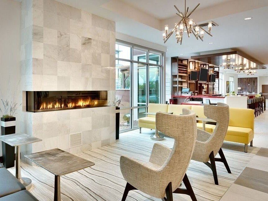 Hotel interior with fireplace and several chairs and tables nearby. A bar and dining tables are at the background.