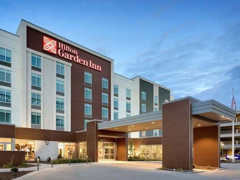 Front angle of a Hilton Garden Inn at dusk with lights illuminating the porte cochere.