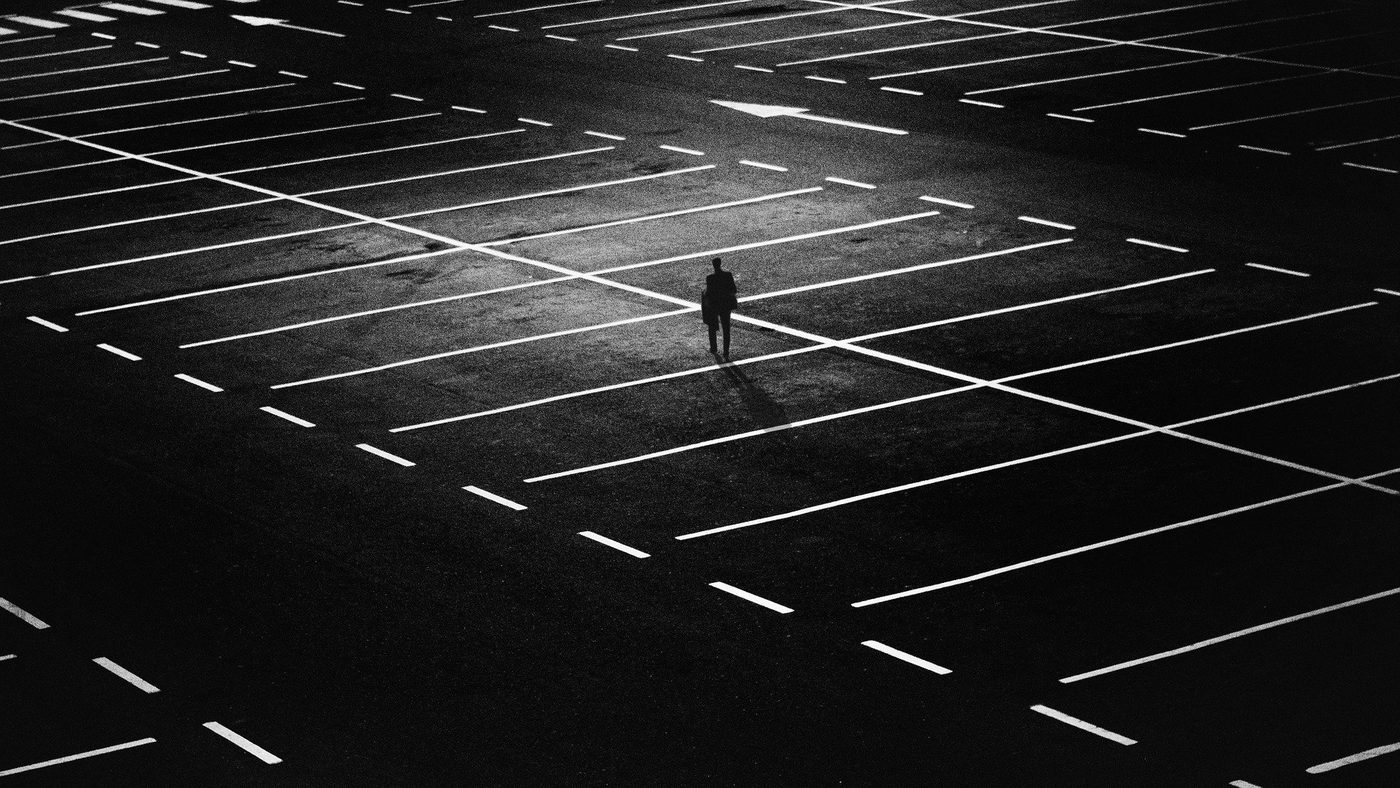 An empty parking lot at night with one man standing in the middle.